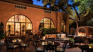 An outdoor patio area with brick flooring, black metal chairs, and tables. There are potted plants and a fire feature in the background. - Rosewood Mansion on Turtle Creek (Dallas)