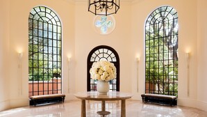 A spacious lobby with a marble floor, a central round table, and three large arched windows with a view of greenery. - Rosewood Mansion on Turtle Creek (Dallas)