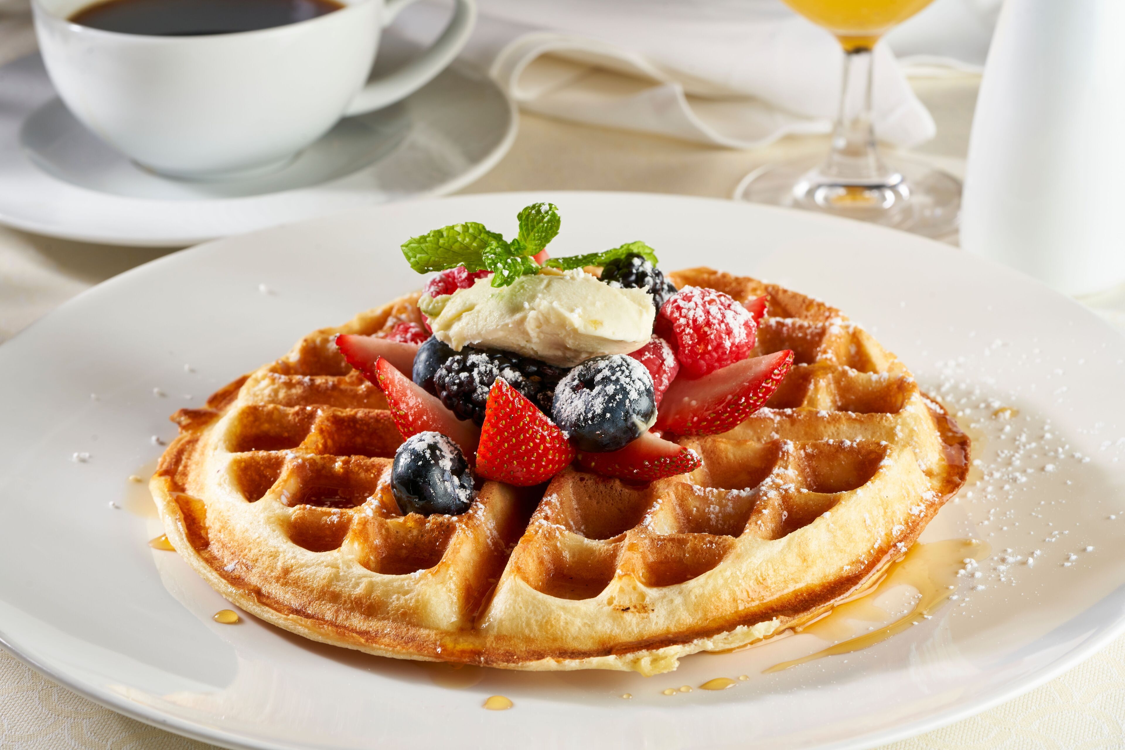 Une assiette de gaufres garnies de crème glacée, de fruits rouges et d’une feuille de menthe.