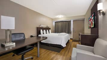 Une chambre d’hôtel avec un lit, un bureau, une chaise et un téléviseur fixé au mur.