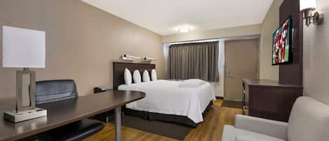 Een hotelkamer met een bed, bureau, stoel en een televisie aan de muur.
