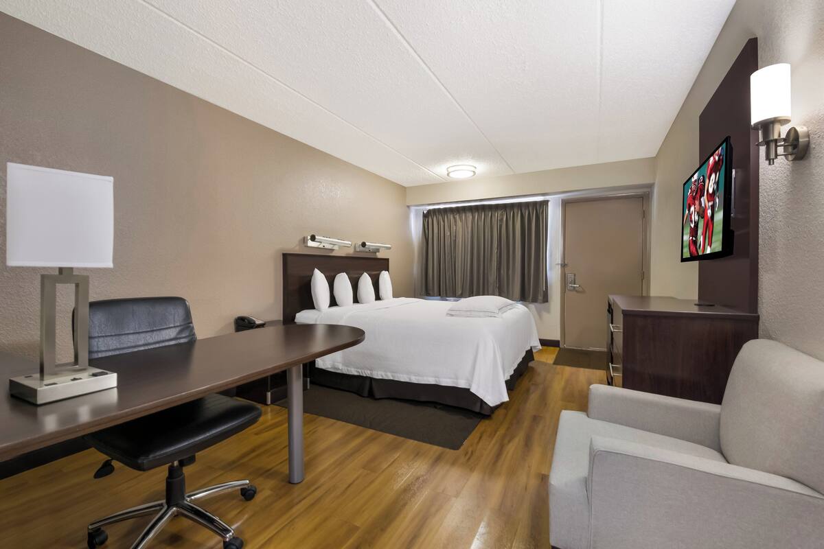 A hotel room with a bed, desk, chair, and a TV on the wall.