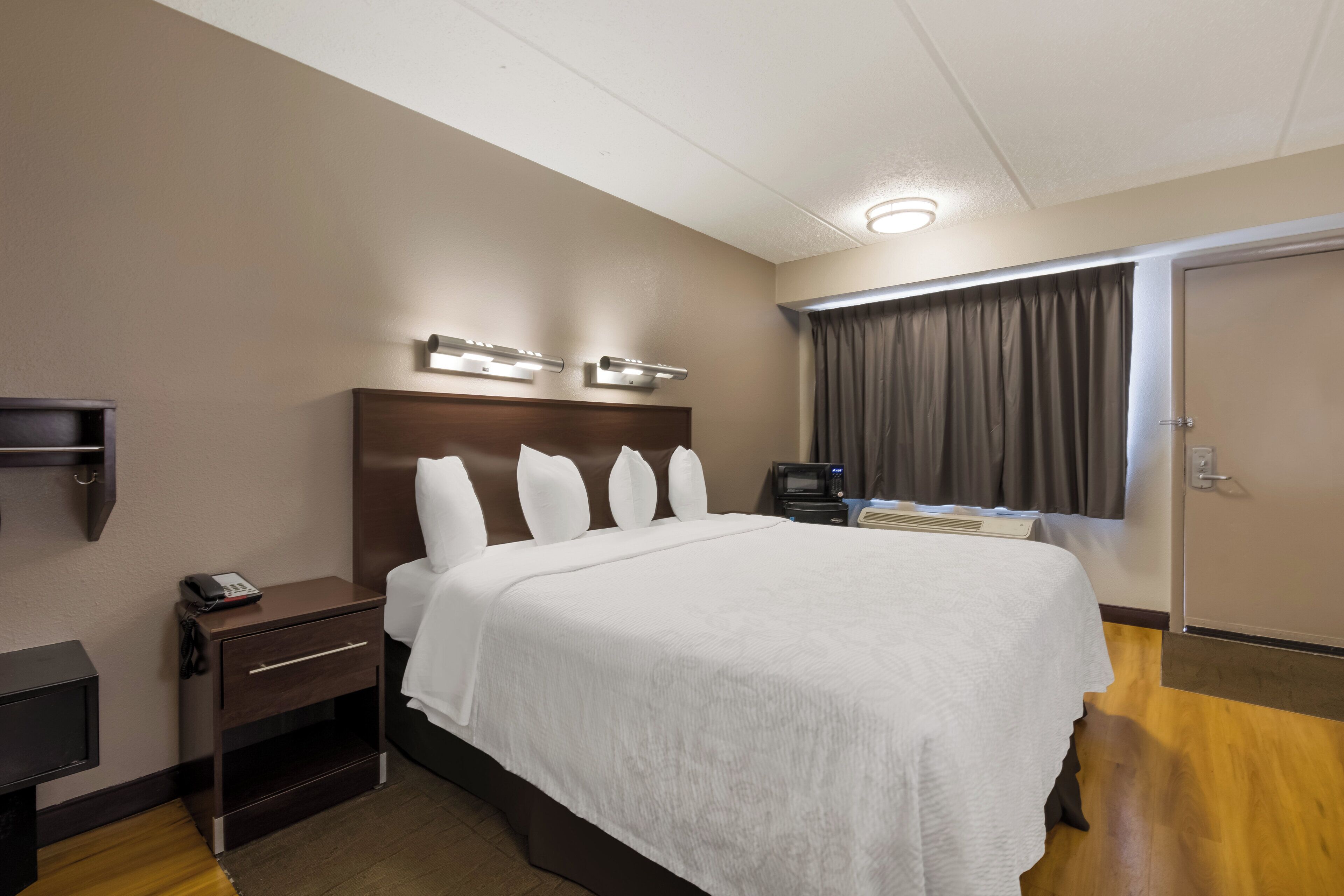 Une chambre d’hôtel avec un grand lit, des tables de chevet, un téléviseur à écran plat, un four à micro-ondes et une fenêtre avec des rideaux.