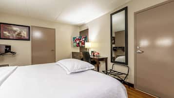 Una habitación de hotel con cama, escritorio, silla, espejo y televisión.