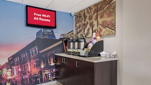 A hotel room with a large mural of a cityscape, a coffee machine, and a sign indicating free Wi-Fi in all rooms. - Red Roof Inn PLUS+ Nashville Airport (Nashville)