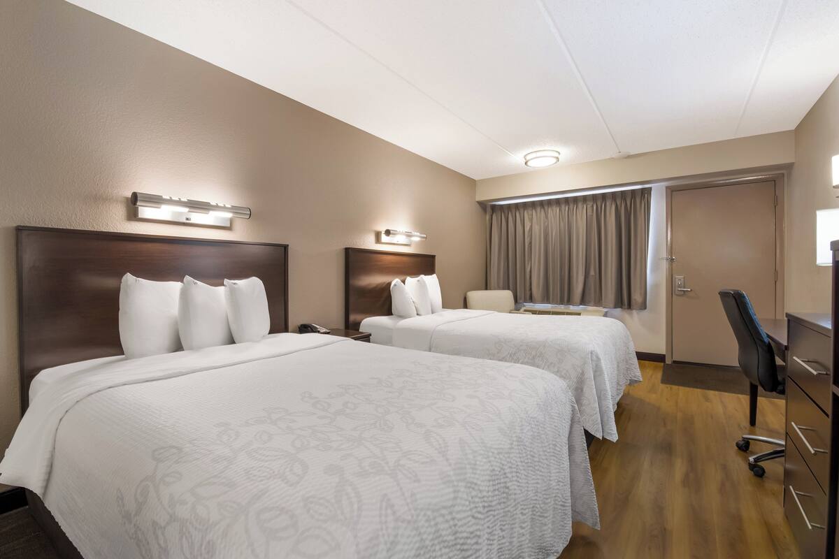 A hotel room with two beds, a desk, and a chair.