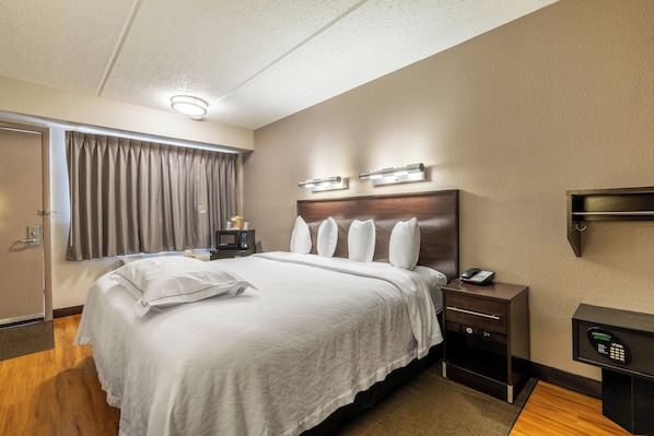 A hotel room with a large bed, a bedside table with a phone, a microwave, and a small cabinet.