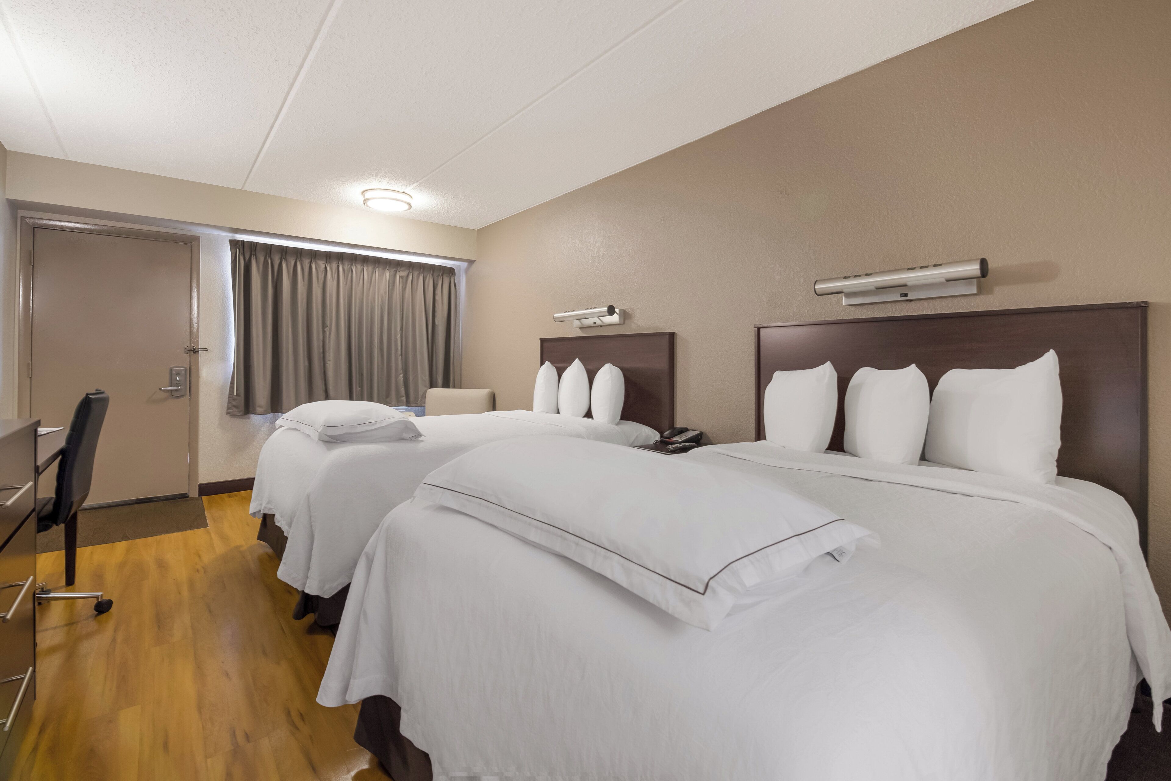 Quarto de hotel com duas camas, uma escrivaninha e uma cadeira.