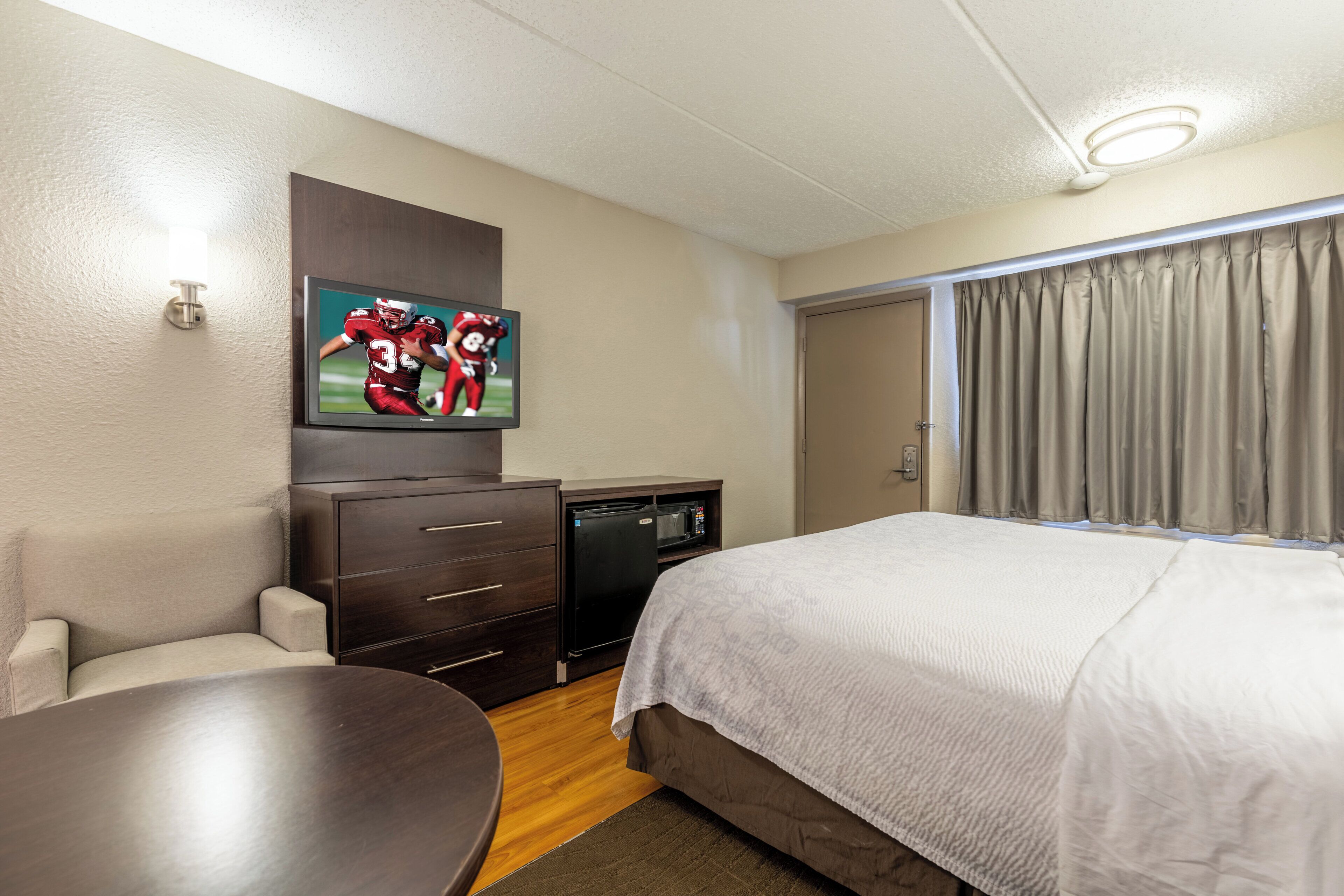 Una habitación de hotel con una cama, un televisor montado en la pared, un escritorio y una puerta.