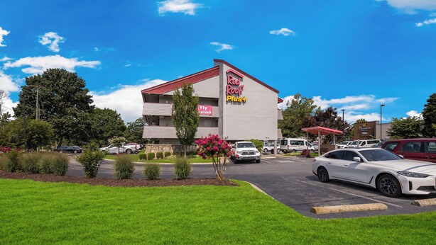 A Red Roof Plus hotel with a parking lot, a white car parked in front, and a clear blue sky. - Red Roof Inn PLUS+ Nashville Airport (Nashville)