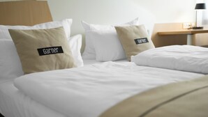 A hotel room with a neatly made bed, two pillows with the name 'Garner', a wooden headboard, and a small bedside table with a lamp.
