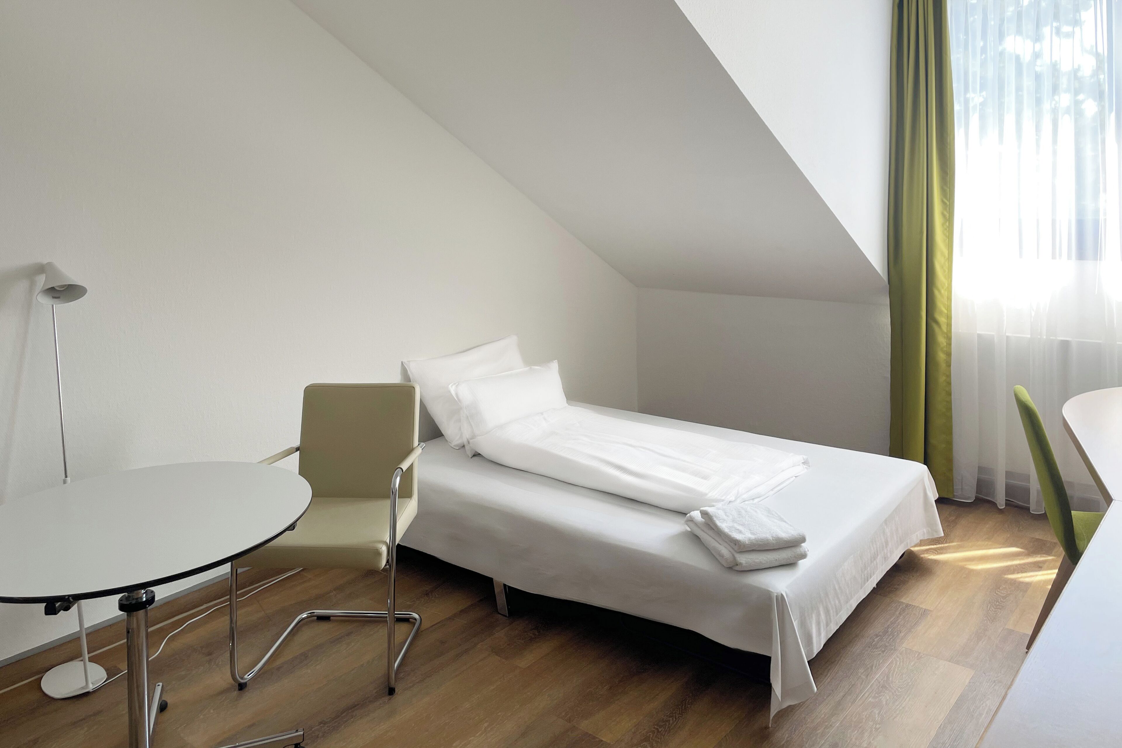 Una habitación de hotel pequeña y moderna con una cama individual, una mesita y una silla.