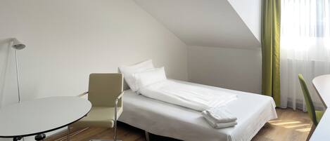 Una habitación de hotel pequeña y moderna con una cama individual, una mesita y una silla.