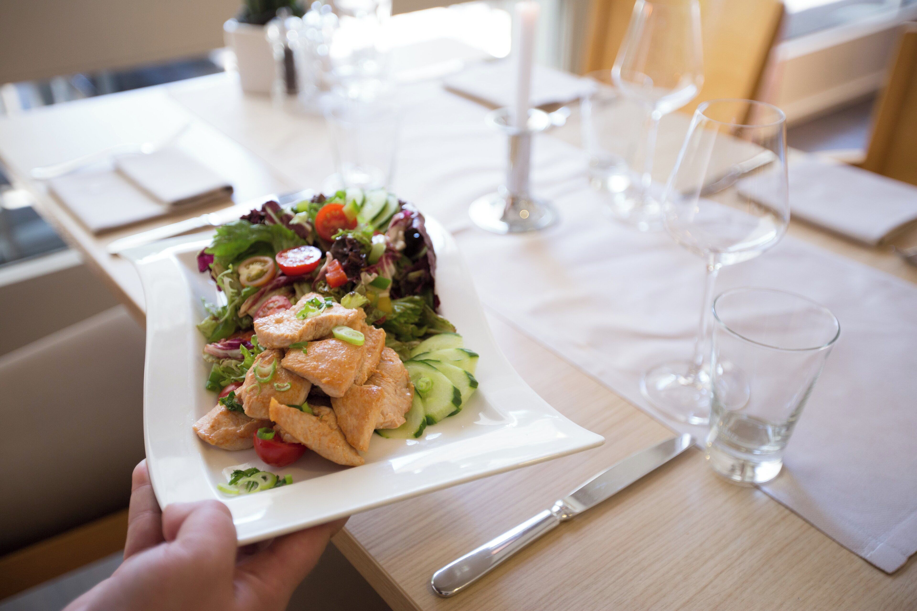 A white plate with a salad and chicken on a wooden table.