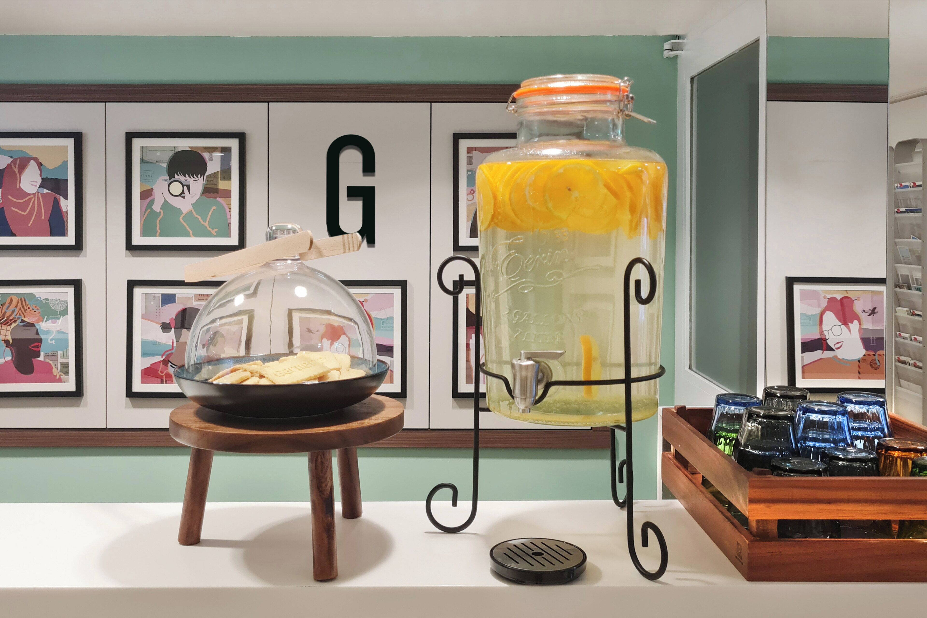 A kitchen counter with a glass jar of lemonade, a bowl of crackers, and a tray of blue glasses.