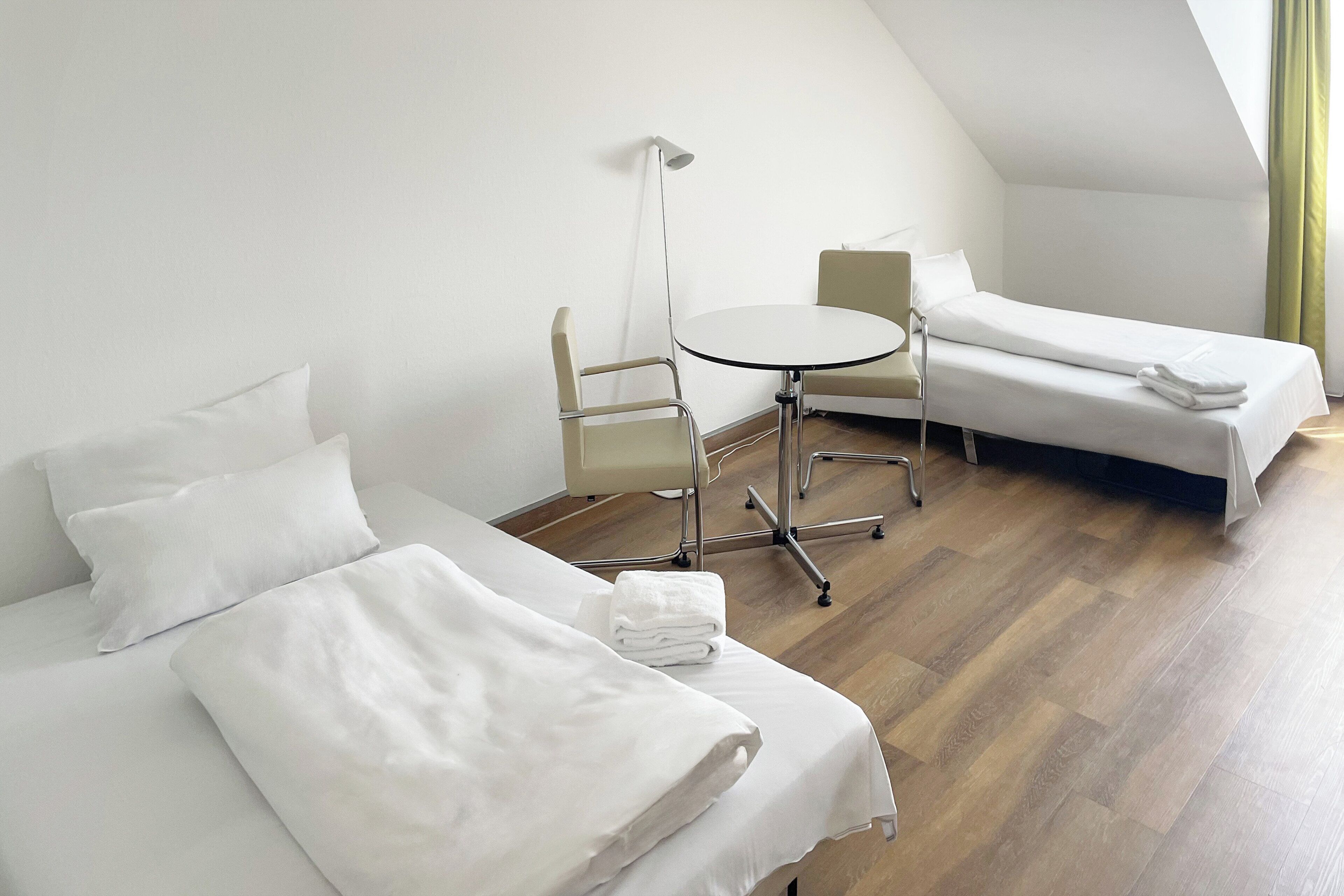 A hotel room with two beds, a round table, and a chair.