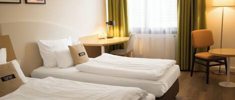 Habitación de hotel con dos camas individuales, un escritorio, una silla y una lámpara.