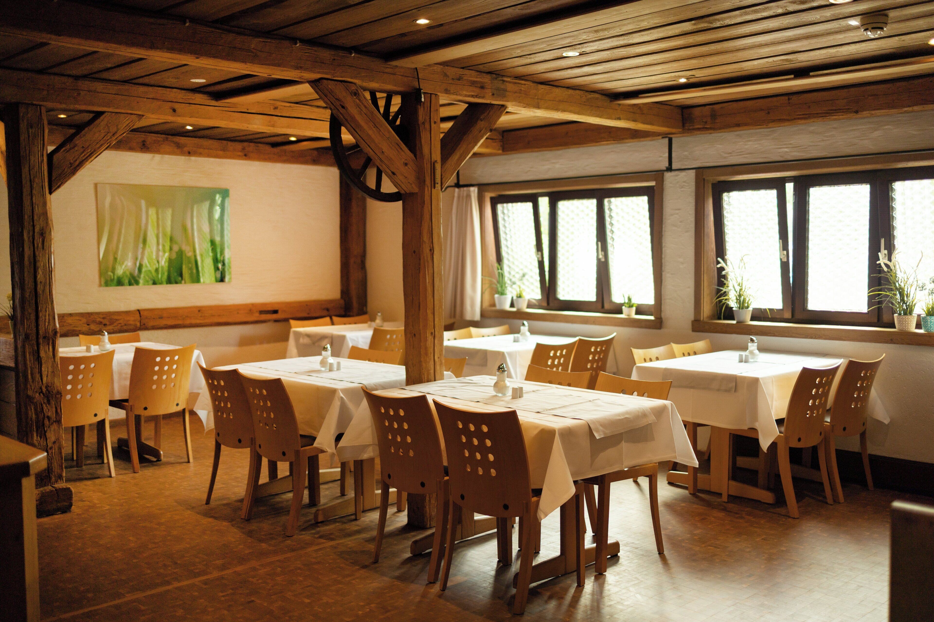 A restaurant with wooden tables and chairs, large windows, and a green abstract painting on the wall.