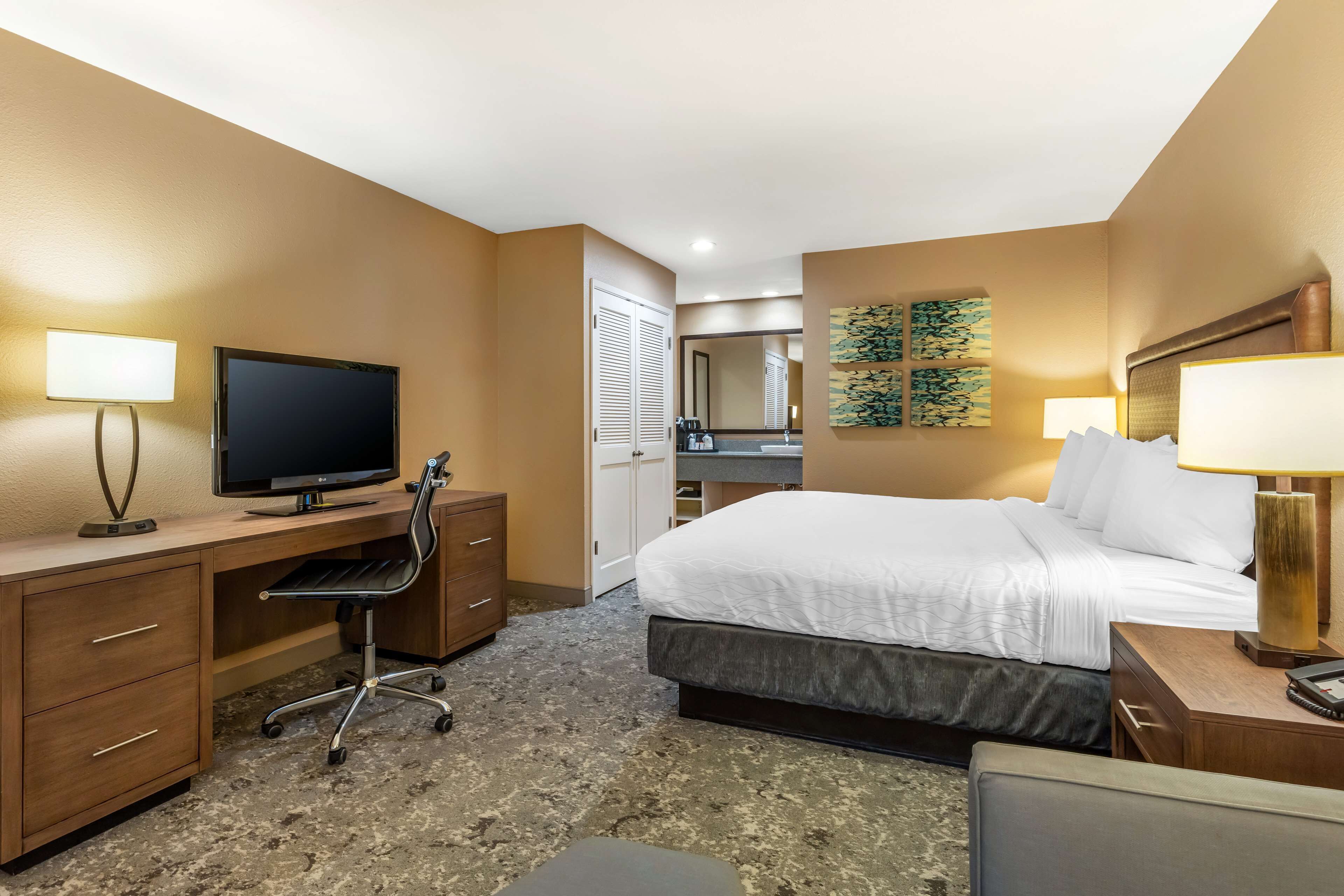 Una camera d'albergo con un letto, una scrivania, una TV e un bagno visibile attraverso una porta aperta.