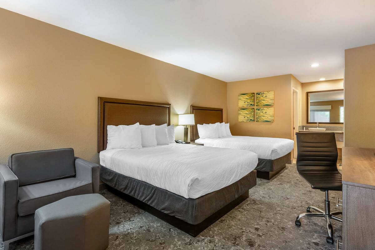 A hotel room with two beds, a desk, a chair, and a sofa.