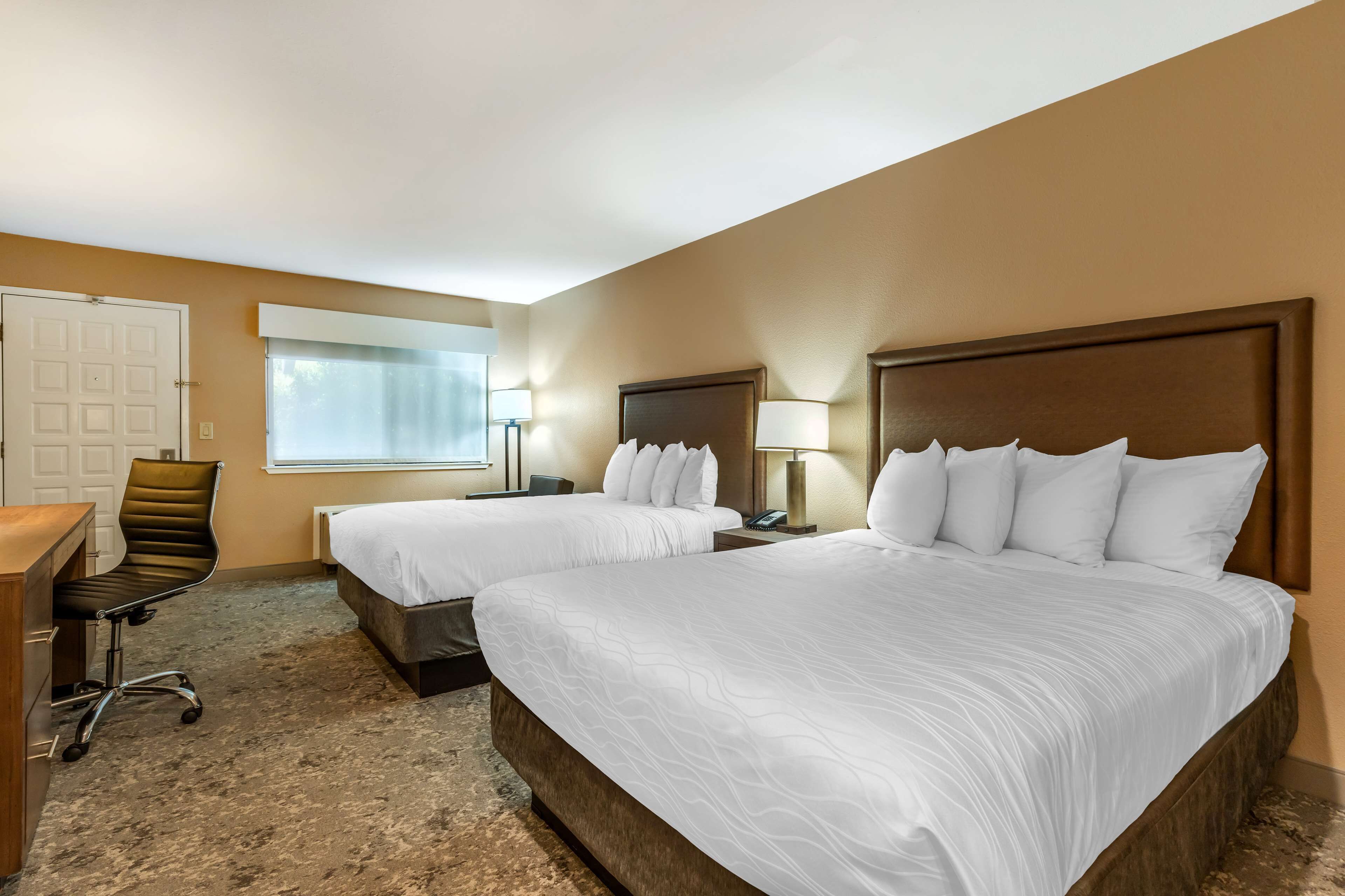A hotel room with two beds, a desk, a chair, and a window with curtains.