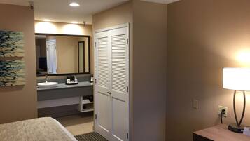 A hotel room with a bed, a bathroom with a sink and mirror, a wardrobe, and a bedside table with a lamp.