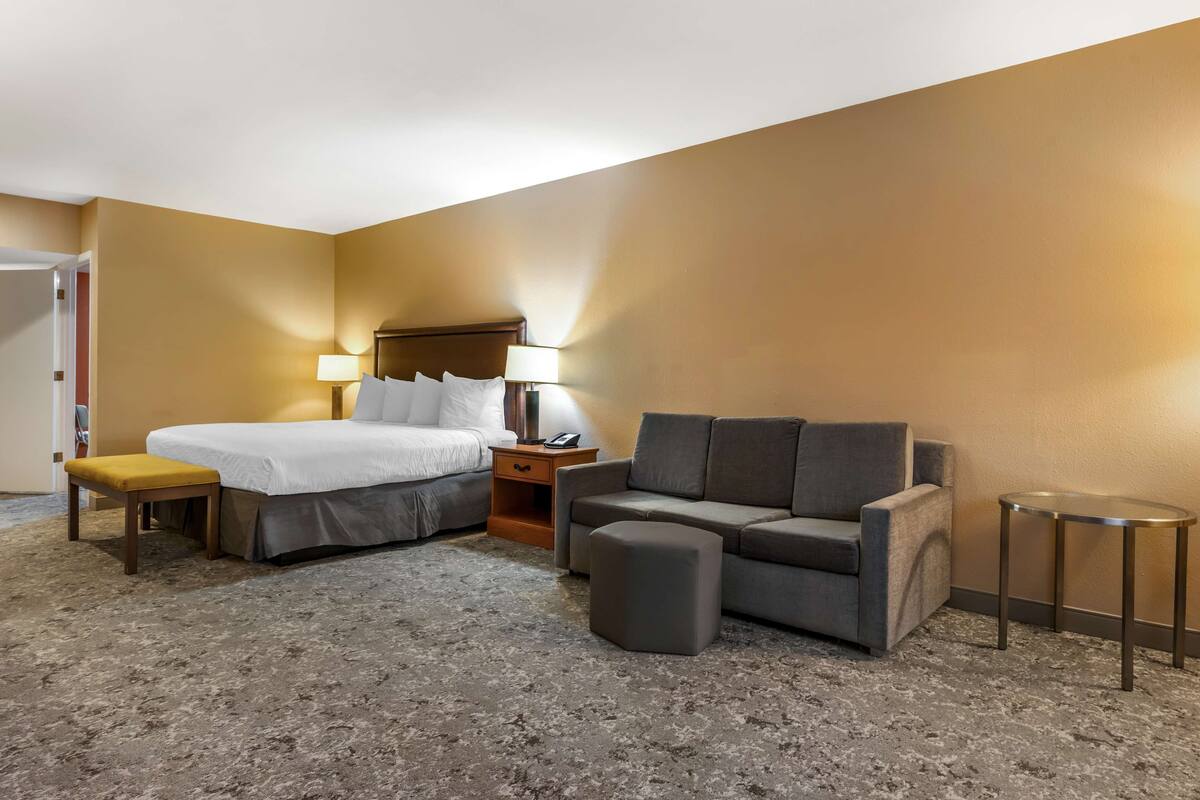 A hotel room with a bed, a sofa, a small table, and a nightstand.