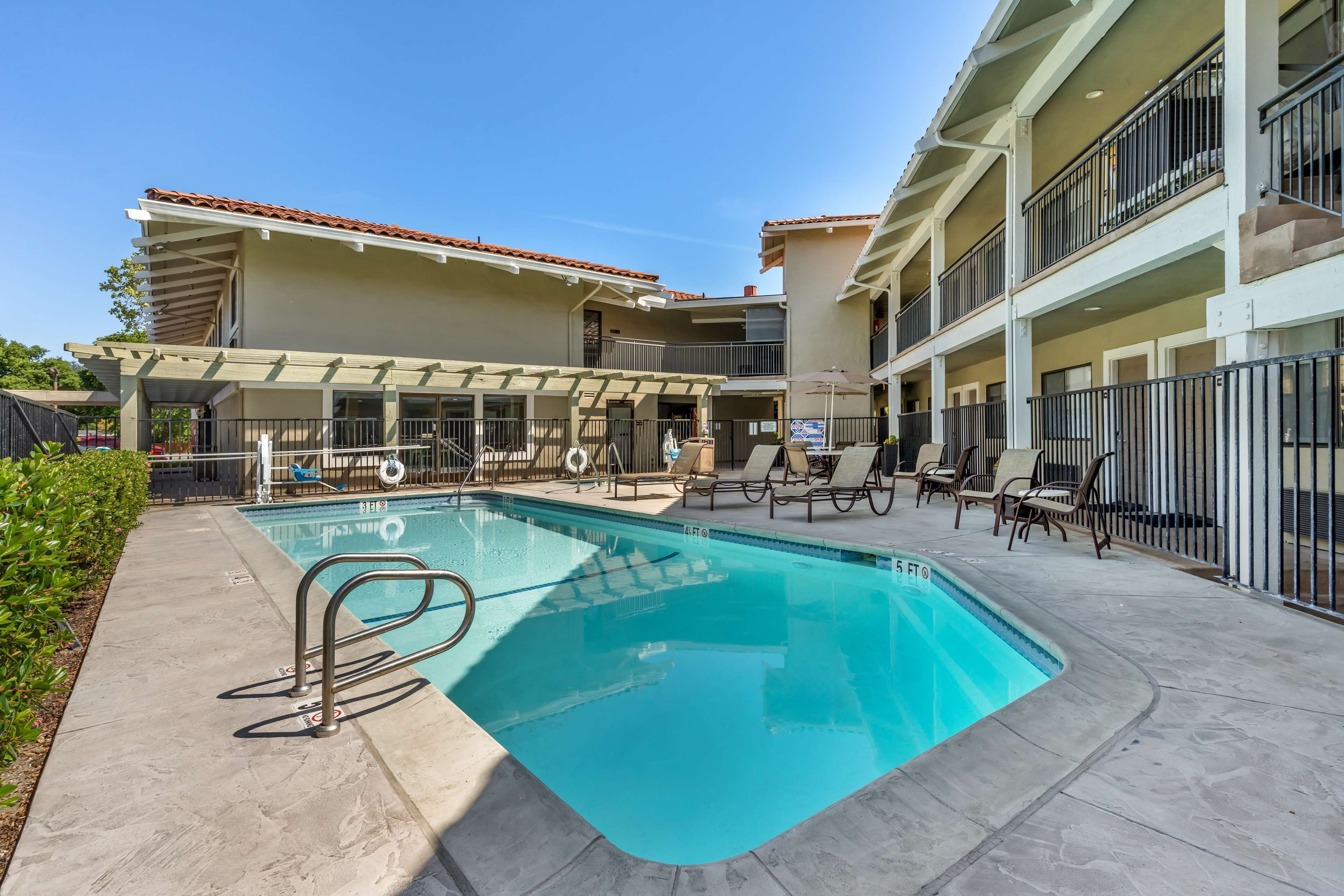 A swimming pool with a sun terrace, lounge chairs, and a multi-story building with balconies.