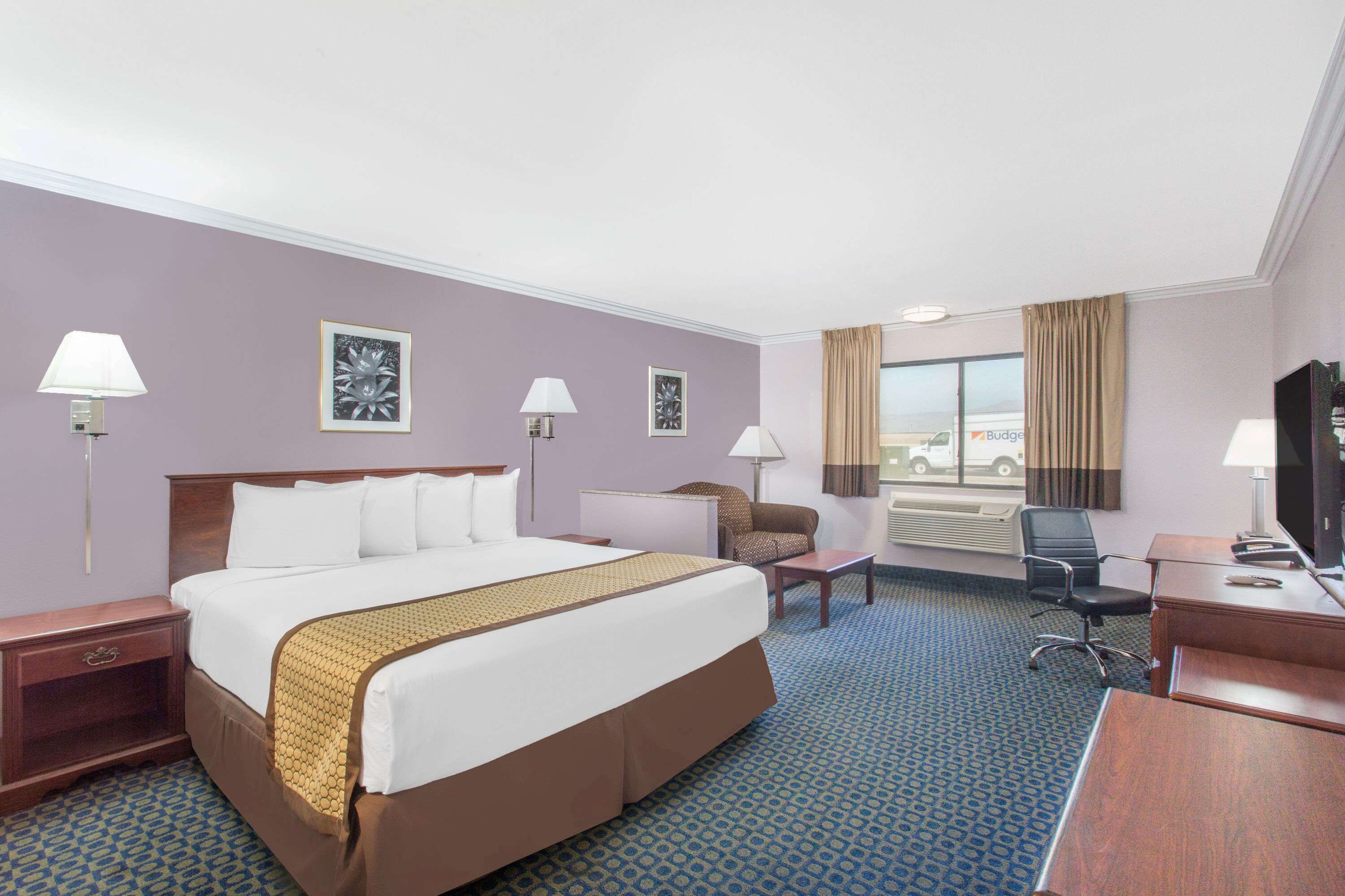 A hotel room with a large bed, a desk, a chair, and a television.