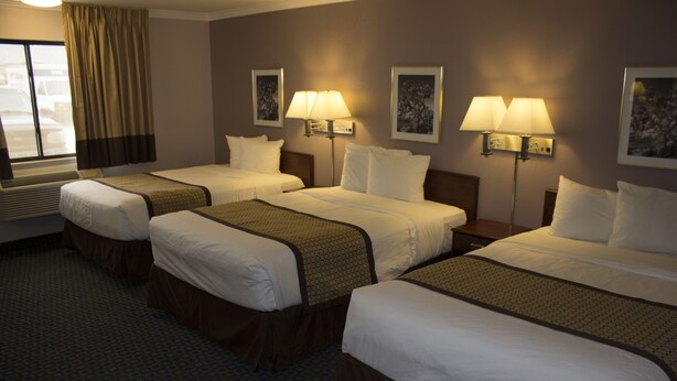 A hotel room with three beds, each with a headboard, a window with curtains, and two wall-mounted lamps.
