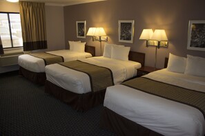 A hotel room with three beds, each with a headboard, a window with curtains, and two wall-mounted lamps.