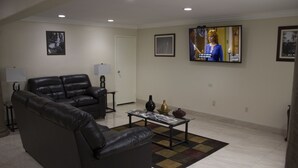 A living room with a black leather sofa, a coffee table with magazines, and a television on the wall.