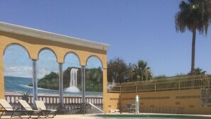 A pool area with lounge chairs, a water feature, and a view of the ocean.