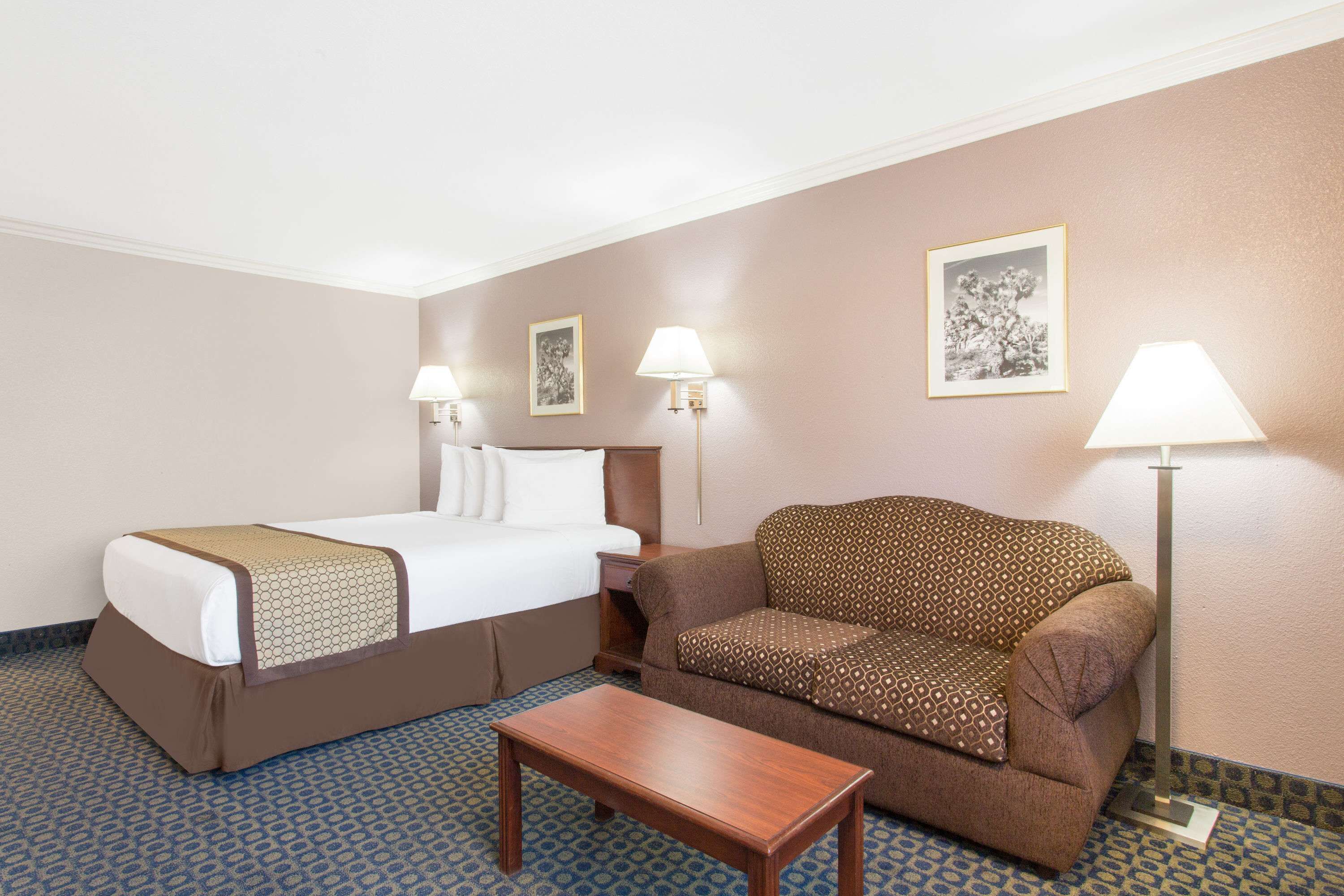 Habitación de hotel con cama, sofá, una mesita y dos lámparas de pared.