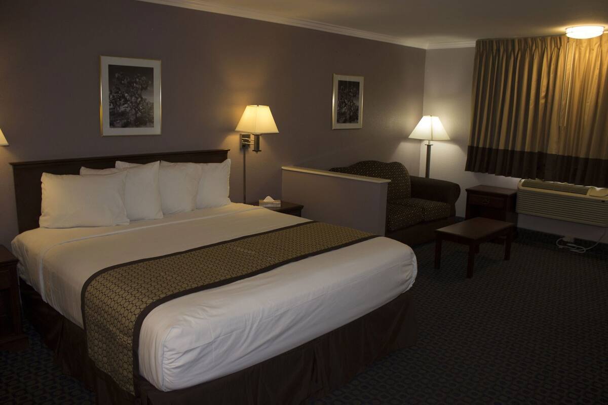 A hotel room with a large bed, two bedside tables, a desk, a chair, and two wall-mounted lamps.