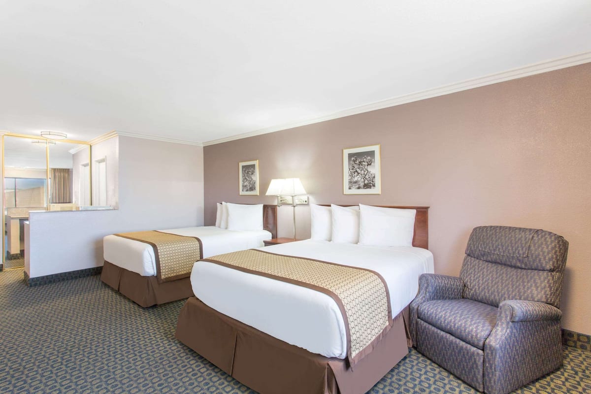 A hotel room with two beds, a chair, a lamp, and framed pictures on the wall.