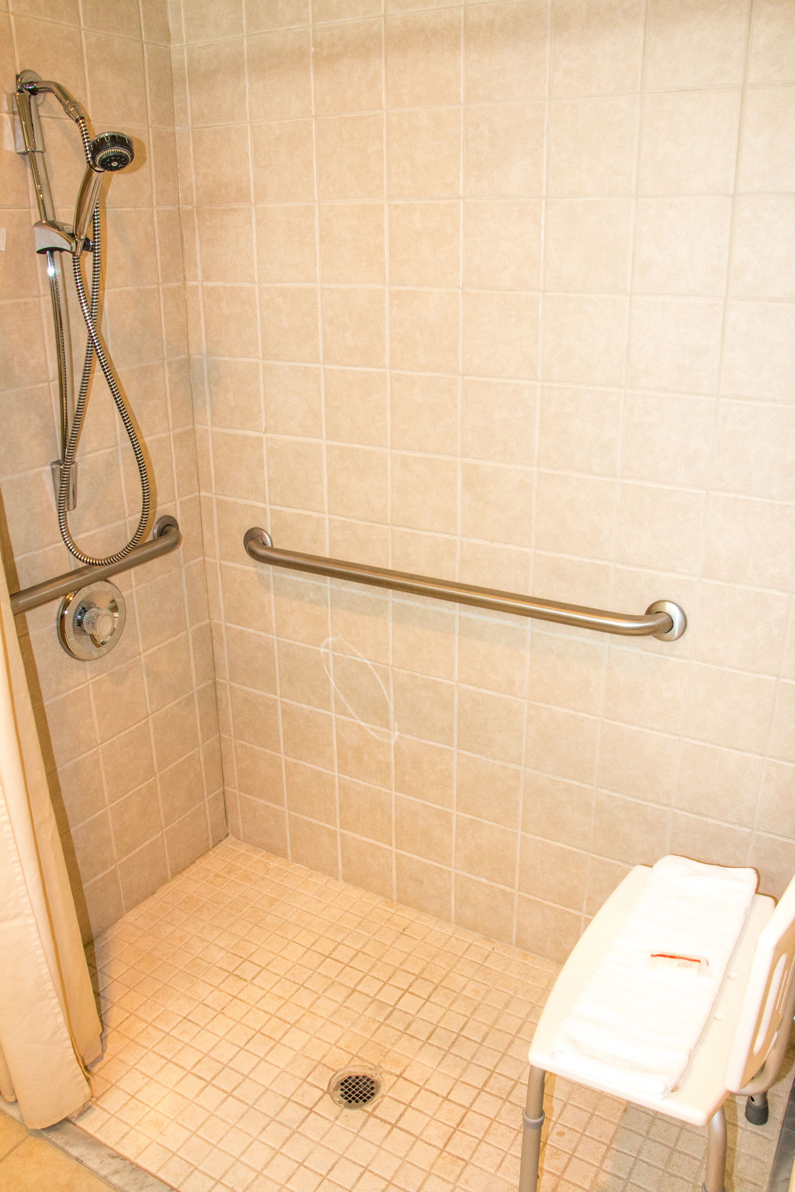 A shower with a grab bar, a white bench, and a tiled floor.