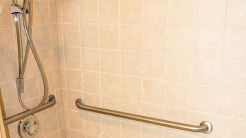 Une douche équipée d’une barre d’appui, d’un banc blanc et d’un sol carrelé.