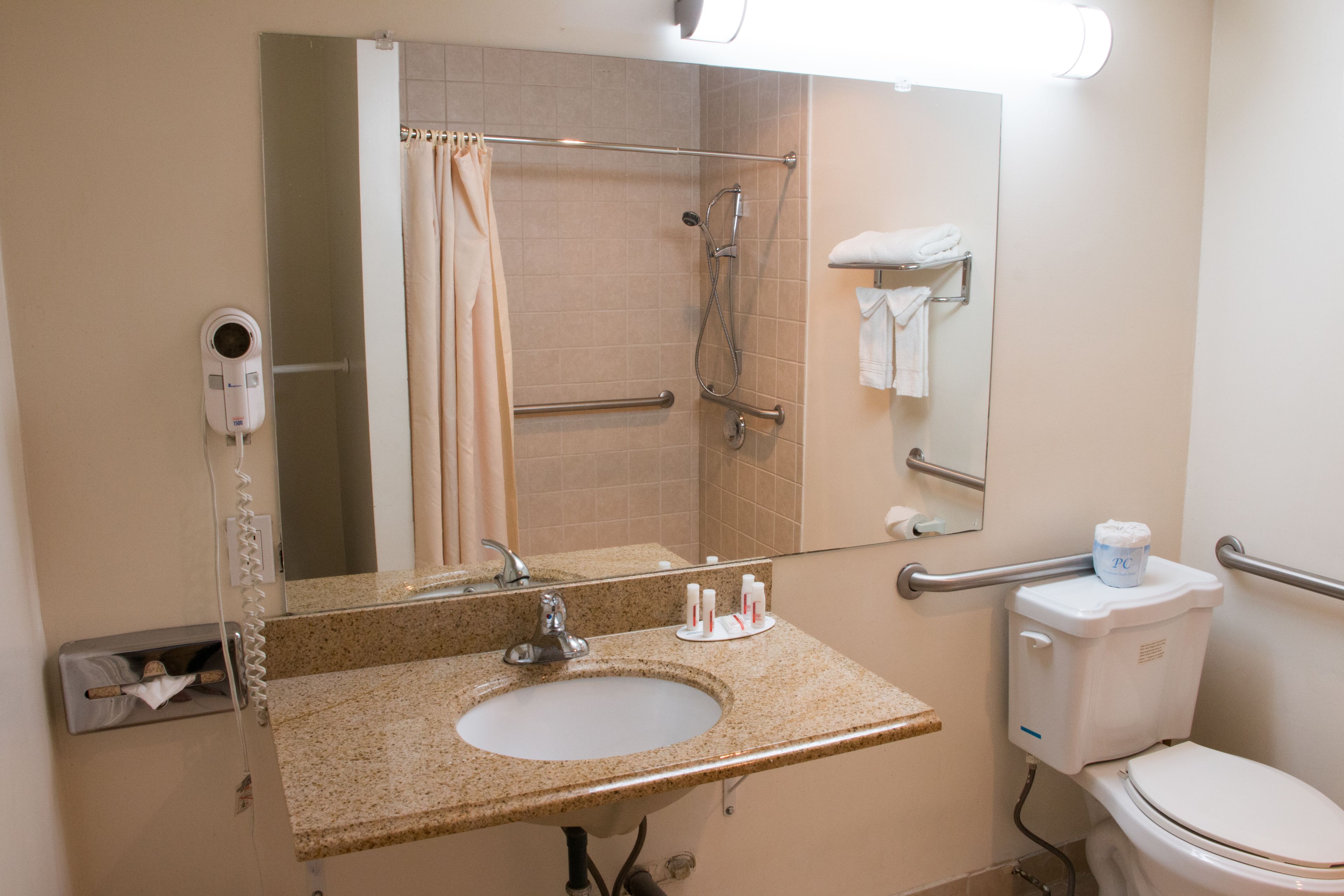 A bathroom with a sink, mirror, shower, toilet, and hand dryer.