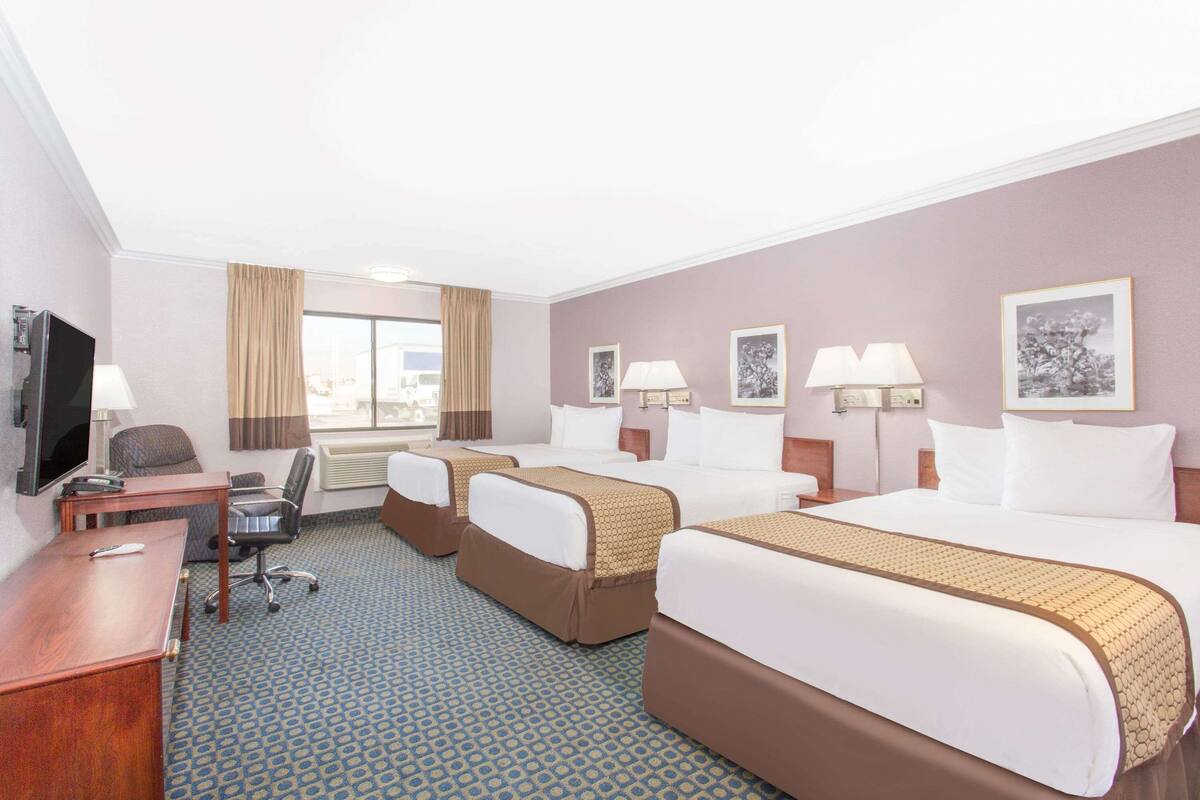 A hotel room with two beds, a desk, a chair, a TV, and a window with curtains.