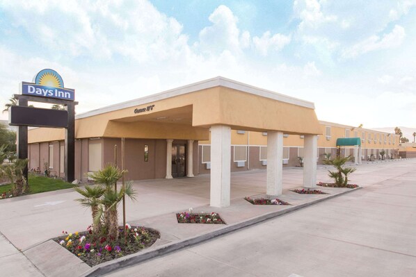 A Days Inn hotel with a central entrance, covered walkway, and flower beds. - Days Inn by Wyndham Indio (Indio)