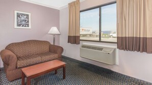 A hotel room with a patterned sofa, a small wooden table, a lamp, and a window with curtains.