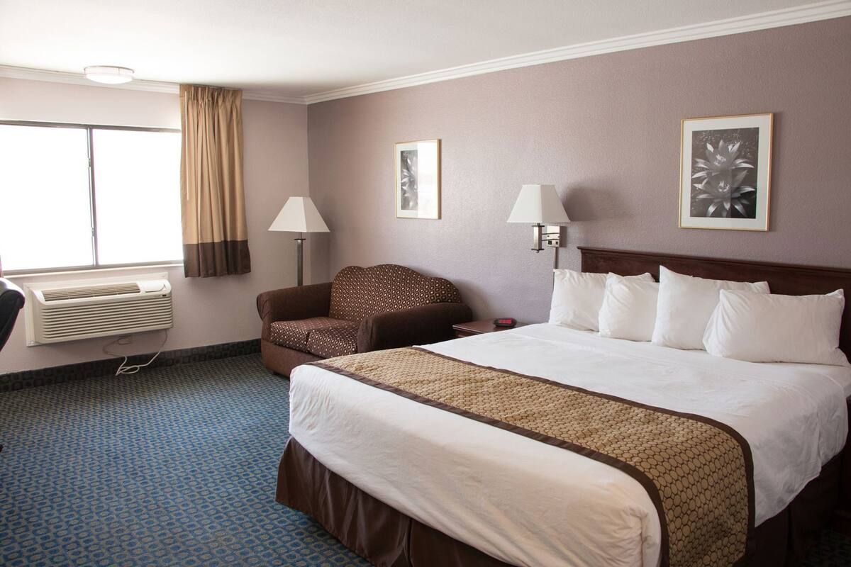 A hotel room with a large bed, a chair, a desk, a lamp, and a window with curtains.