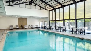 An indoor swimming pool with clear blue water, surrounded by lounge chairs and tables.