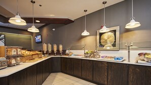 A modern kitchen with a built-in counter, hanging pendant lights, and a variety of food items displayed.