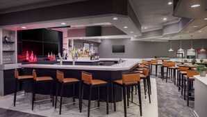 A modern bar area with a central island, bar stools, and a variety of bottles.