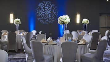 Un salón de banquetes con mesas redondas, sillas blancas y centros de mesa florales.