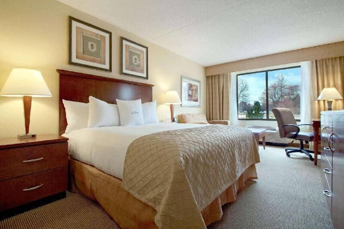 A hotel room with a bed, bedside tables, lamps, a desk, and a chair.
