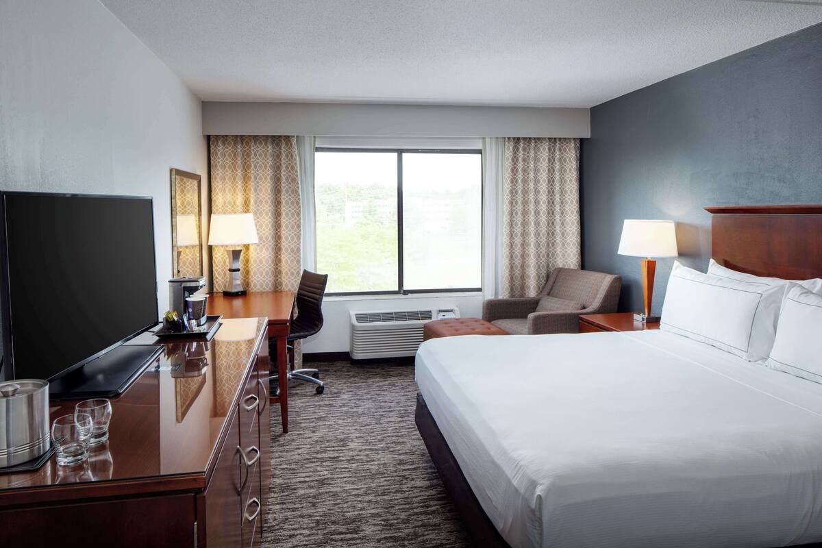 A hotel room with a large bed, a desk with a TV, a chair, and a window with curtains.