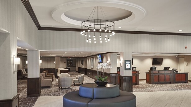 A modern lobby with a central seating area, a reception desk, and a chandelier.